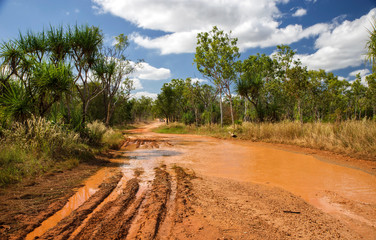 Fototapeta na wymiar Western Australia – Flooded Outback gravel road after 4WD car crossing the waterhole with muddy water at the savanna