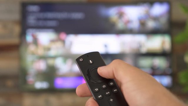 Male hand holding the TV remote control and changing TV channels