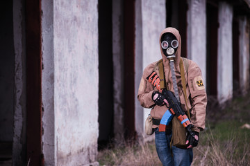 Fototapeta premium Armed stalker warrior in gas mask in front of lost destroyed building