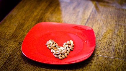 Fried almond grains are placed on a red plate in the form of an shape heart. The plate stands on a wooden table.