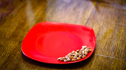 Fried almond grains are placed on a red plate. The plate stands on a wooden table.