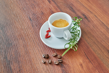 Italienischer Espresso in einer weißen Tasse mit Rosmarin, Goji Beeren und Kaffee Bohnen auf braunem Hintergrund.