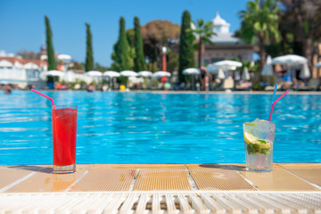 Fototapeta na wymiar Two refreshing cocktails Mojito and Cosmopolitan stand on the edge of the pool in the summer heat with a blurred background. The concept of rest and travel is an expensive holiday. place for text.