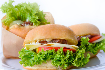 Burger is delicious American fast food. Closeup group of set three hamburger made from pork or beef, green lettuce bread onion and tomato in a paper bag and dishes on a white table background at home
