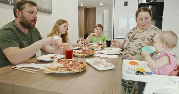 Family having dinner together at home. Overweight parents speaking with each other while feeding baby and having dinner with children during quarantine at home