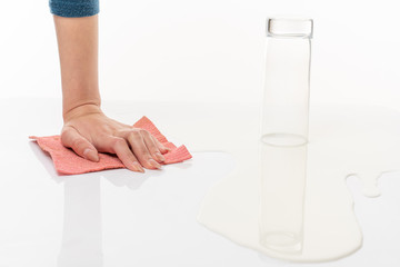 Inverted empty glass among the spilled milk and female hand with rag