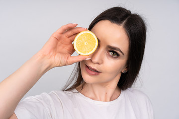 A young girl with dark hair holding a lemon instead of eyes, the concept of beauty and health