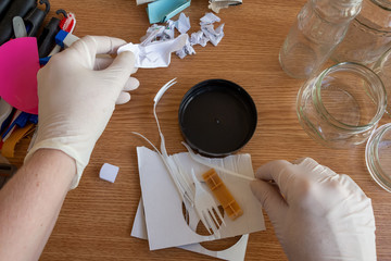 A person divides the trash lying on the wooden table into three groups: paper, plastic and glass....
