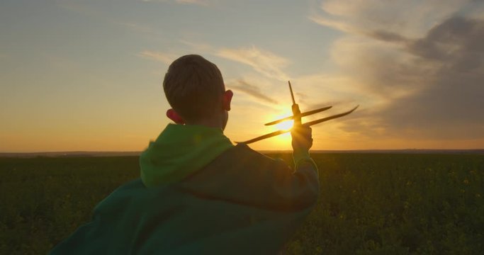 A boy is running across a field with a plane in his hand. Sunset. 4K