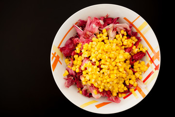 Salad with corn on black table, top view
