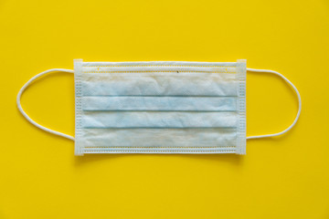 Blue medical protective mask isolated on yellow background. Disposable 3-ply medical mask to cover the mouth and nose to prevent coronavirus. Procedure mask from bacteria. Coronavirus quarantine.