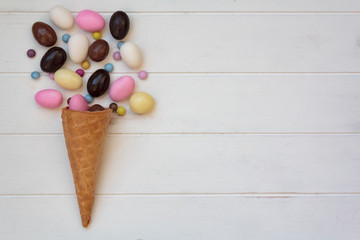 Top view of ice cream cone with sweet almond eggs on white wooden table with copy space