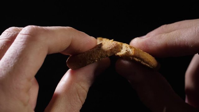 Men's fingers hold a cookie and then break it in half