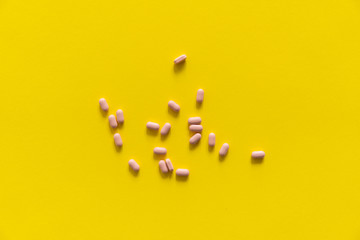 Pink pills on yellow background. Medicine, medication, painkillers, tablet, medicaments, drugs, antibiotic, vitamin, treatment. Pharmacy theme. Top view on the pills scattered on the white surface.