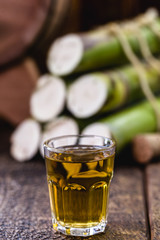 Glass of drink of high quality distilled alcohol. With pieces of sugar cane in the background. Brazilian cachaça (called pinga), drip, golden rum from Brazil.