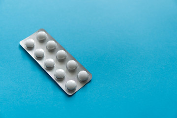 Top view on the pills in the package. White pills on blue background. Medicine, medication,...