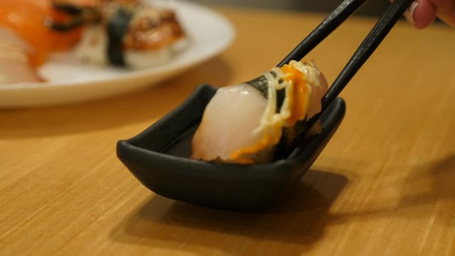 Eating white fish sushi at restaurant, take one piece and put into soy sauce in small dish. Closeup shot of tiny plate