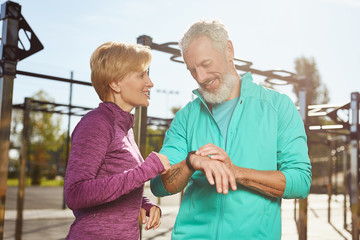 Fitness app. Happy mature family couple in sports clothing checking training results while exercising together outdoors, they are looking at smartwatch and smiling