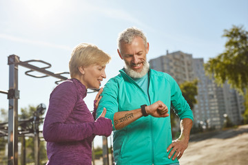 Great results. Happy mature family couple in sportswear looking at smartwatch and checking training...