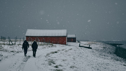 Two men walk in the snow along path by the sea