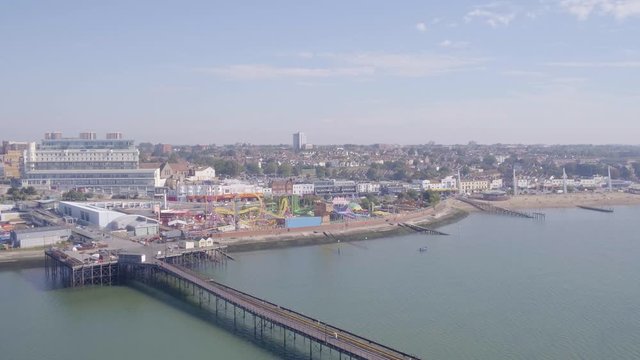 Drone or aerial pull back reveal of Southend pier and beach showing the promenade with hotels, funfair, shops and arcades