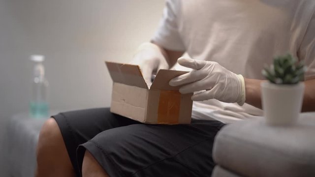 Man packing small package in small box, male distributor packing carton parcel receive goods purchase postal shipping delivery, covid-19 crisis, express shipment, man wear white gloves, quarantine