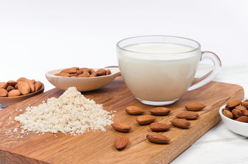 Almond milk in cup with almond flour and nuts on white background