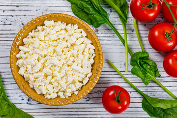Feta Crumbled Cheese with Spinach and Tomatoes on White Wooden Background. Selective focus.