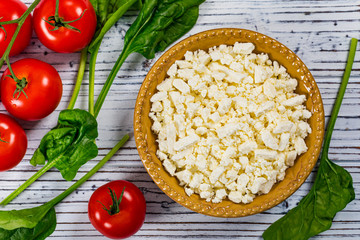 Feta Crumbled Cheese with Spinach and Tomatoes on White Wooden Background. Selective focus.