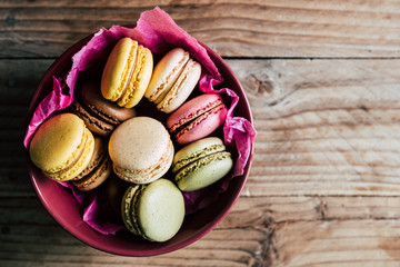 Macarons colorés dans un bol rose sur un fond en bois