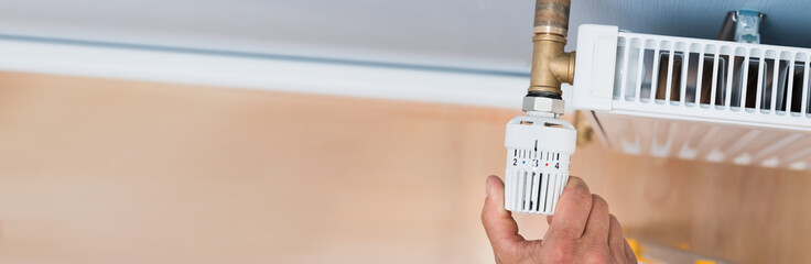 Person Adjusting Temperature Of Radiator Thermostat