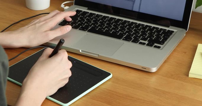 Female hands of Graphic designer at work from home with digital tablet and laptop. Young artist drawing illustration using a pen, graphic tablet and image editor on the computer