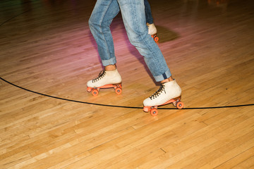 Legs of people roller skating in a wood skate ring.