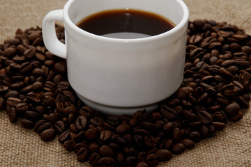 heart made from coffee beans top in the center a white cup with coffee.