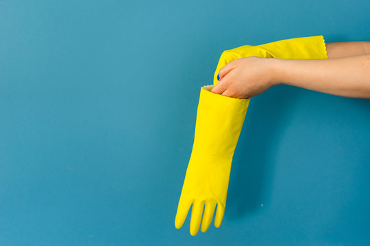 Close up on hand of unknown caucasian woman female girl putting on protective yellow rubber gloves to clean or disinfection against blue wall background in day