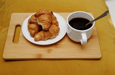 cup with coffee with croissants on a wooden tray on the pillow.