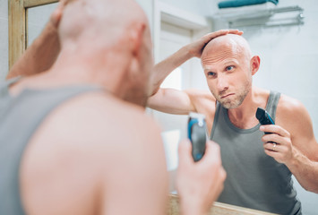 Hairless man touching his new style bald head haircut he made using an electric rechargeable...