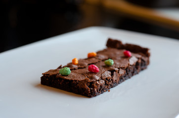 Homemade brownie on white plate. Brownie on black counter. Brownie with decoration. Brownie with smiley.
