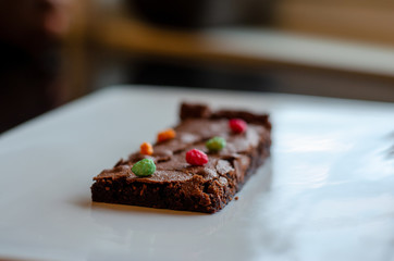 Homemade brownie on white plate. Brownie on black counter. Brownie with decoration. Brownie with smiley.