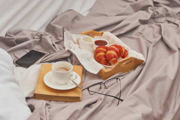 Breakfast on a crumpled bed, coffee, croissants, book, mobile phone
