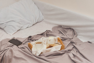 Fototapeta na wymiar Breakfast on a crumpled bed, coffee, croissants, book, mobile phone