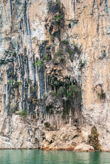 Wuchan, China - May 7, 2010: Dawu or Misty Gorge on Daning River. Packs of stalactites hang form brown cliffs in front of caves above emerald geen water.