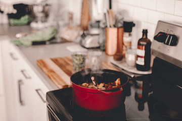 Lady cooks dinner for family. Dutch oven on stove top. Lifestyle kitchen. Stewed potatoes. Seasoning with salt, stiring meal. Hot meal. Cook process. Dinner preparation. Kitchen towel. Red dutch oven