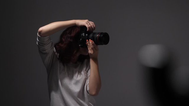 a young girl, a photographer, works in the studio, takes pictures with a big black camera with flash, after which she checks the photos and smiles, laughs