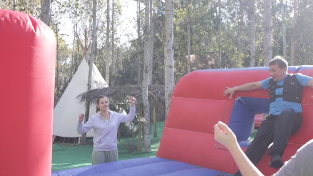 Two cheerful men having funny battle by big boxing gloves on inflatable arena at amusement park