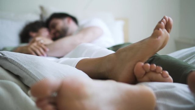 closeup of couple in bed playful with feet spbd. man and woman lying togetherness and relaxing in bedroom. concept indoors, girlfriend, boyfriend. lying comfortably talking