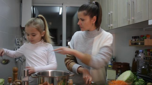 Happy mother and little daughter preparing soup together at home,  cut vegetable 
