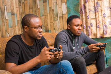 two handsome africans guys sitting on the couch playing video games with joystick, game pad, pad