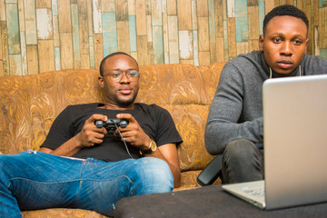 two handsome africans guys sitting on the couch playing video games with joystick, game pad, pad