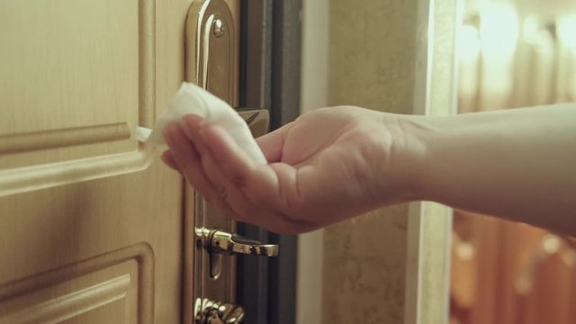 Surface sanitation. Coronavirus precaution. Woman hand sterilizing door handle with alcohol wet wipe.
